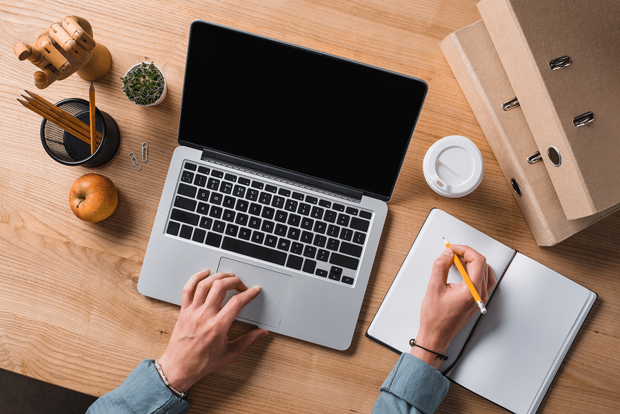 staff member writing website content for client on laptop, with pen and paper for notes